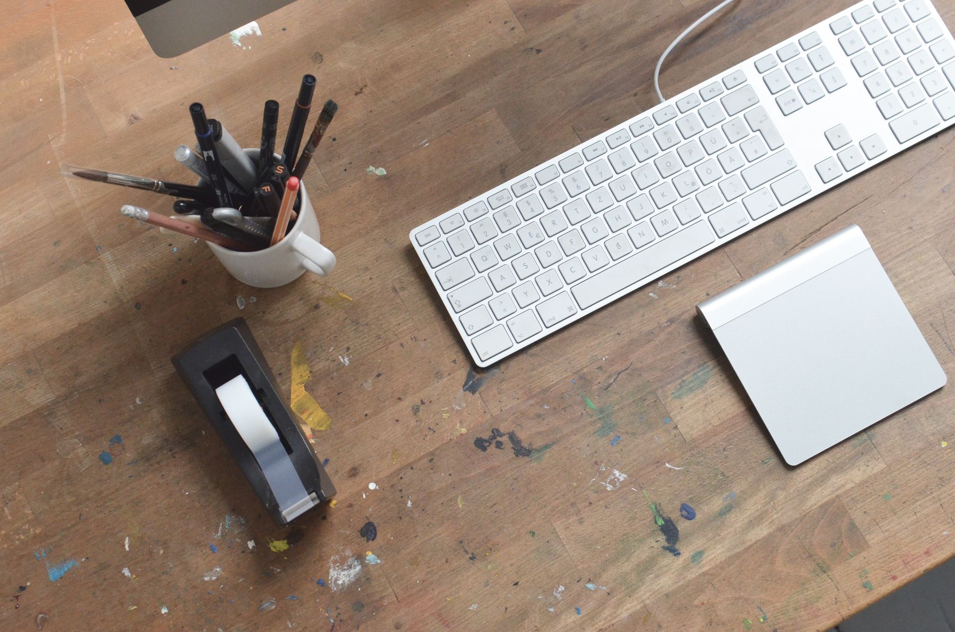 Top-down view of a laptop keyboard on a wooden desk with pens in a cup.